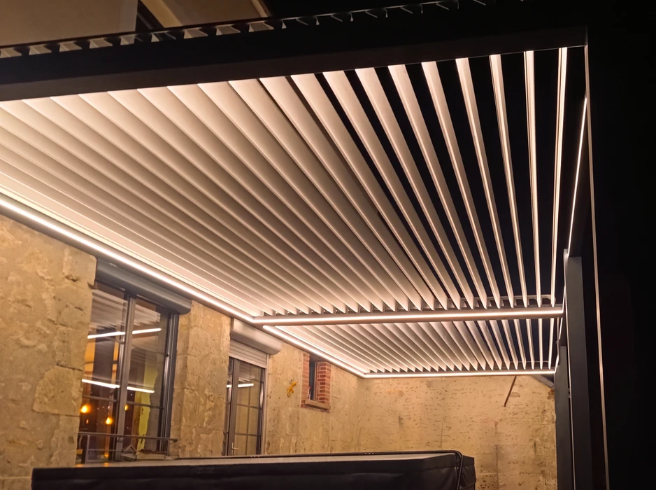 Pergola bioclimatique à lames orientables en aluminium blanc, éclairée de nuit par des bandeaux LED intégrés dans les rails périmétriques