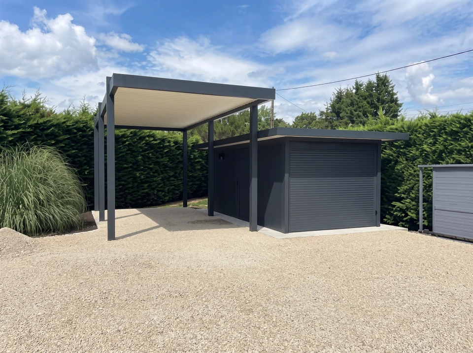 Carport moderne en aluminium anthracite, structure tubulaire avec couverture en plaques ondulées blanches, accolé à un abri de jardin fermé avec porte battante et volet roulant