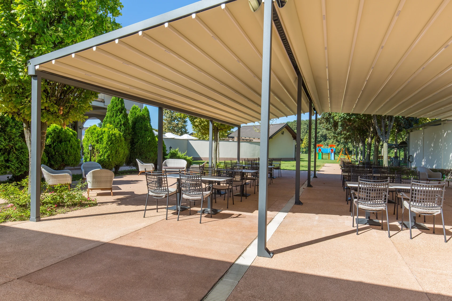 Pergola bioclimatique aluminium anthracite sur terrasse composite grise, avec lames orientables blanches et stores enrouleurs latéraux beige
